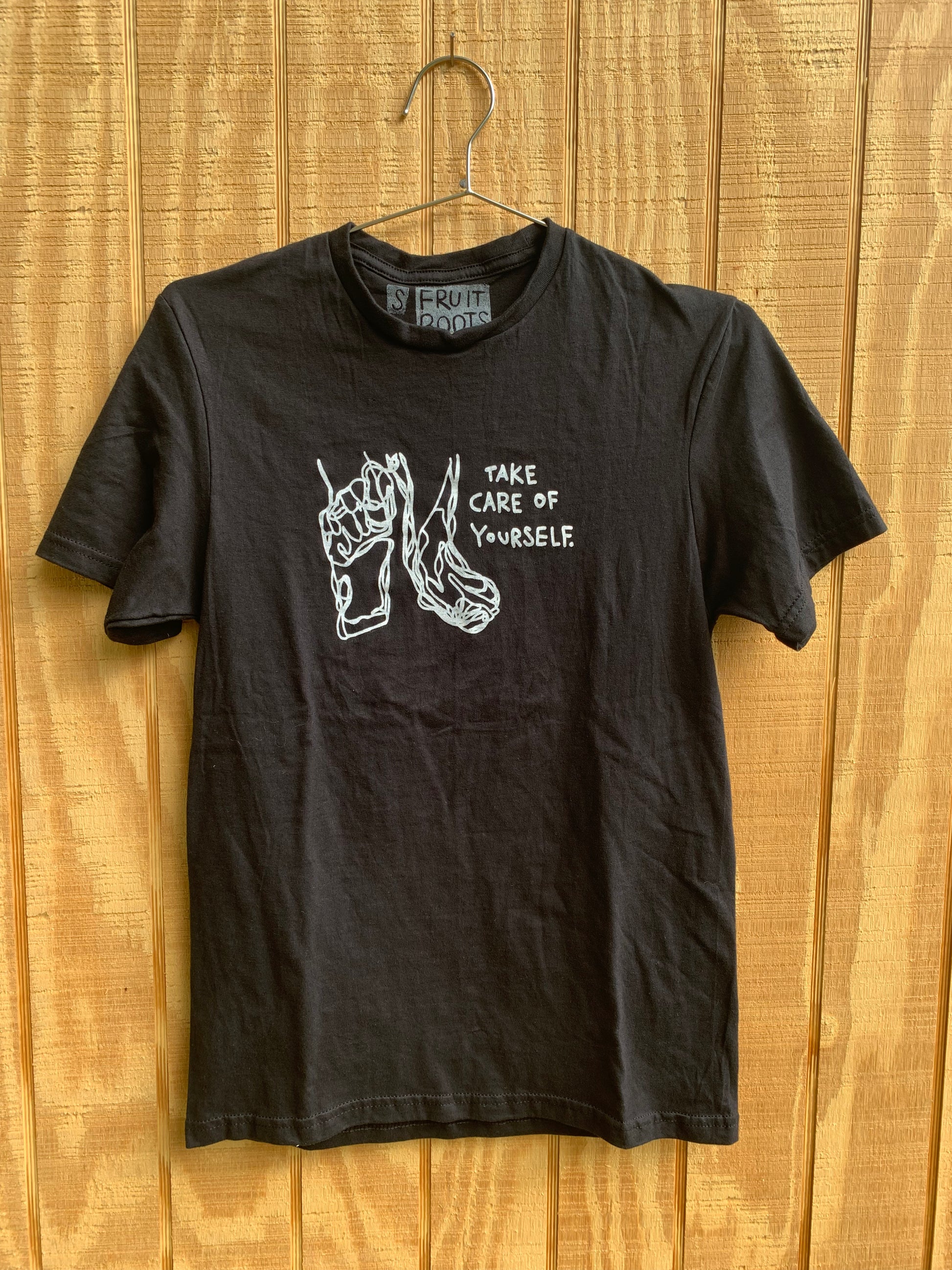 Black T Shirt with white blind contour drawing of feet and white text that reads "take care of yourself"