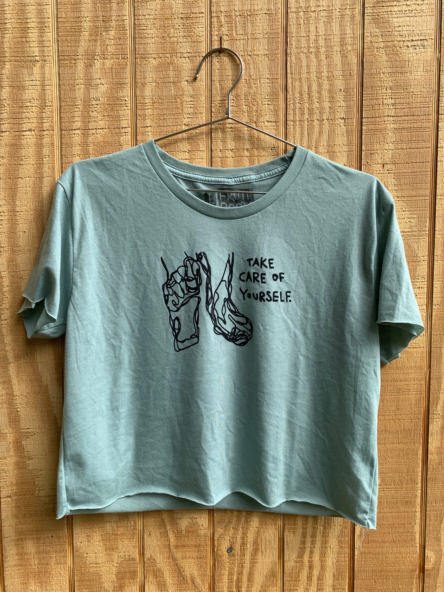 Teal crop top with black blind contour drawing of feet and black text that reads "take care of yourself"